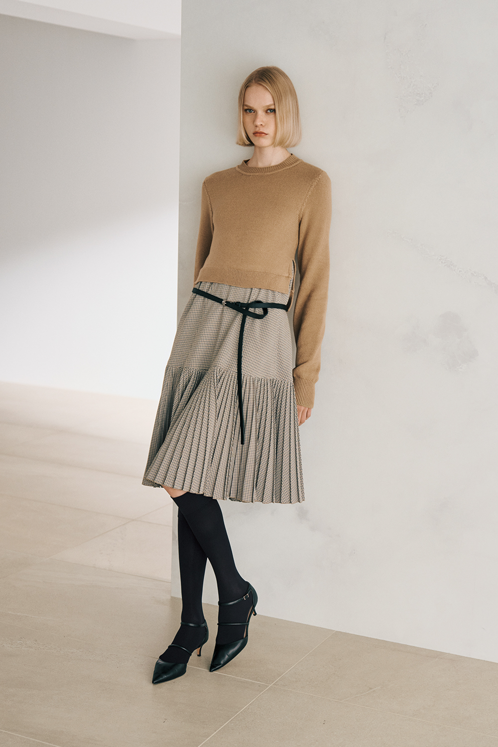 The model is wearing a black jacket, black pants, and a black belt.