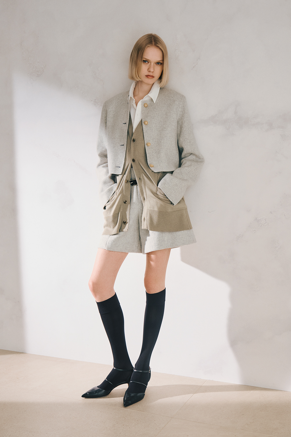 The model is wearing a light gray jacket and pants set and black pumps.