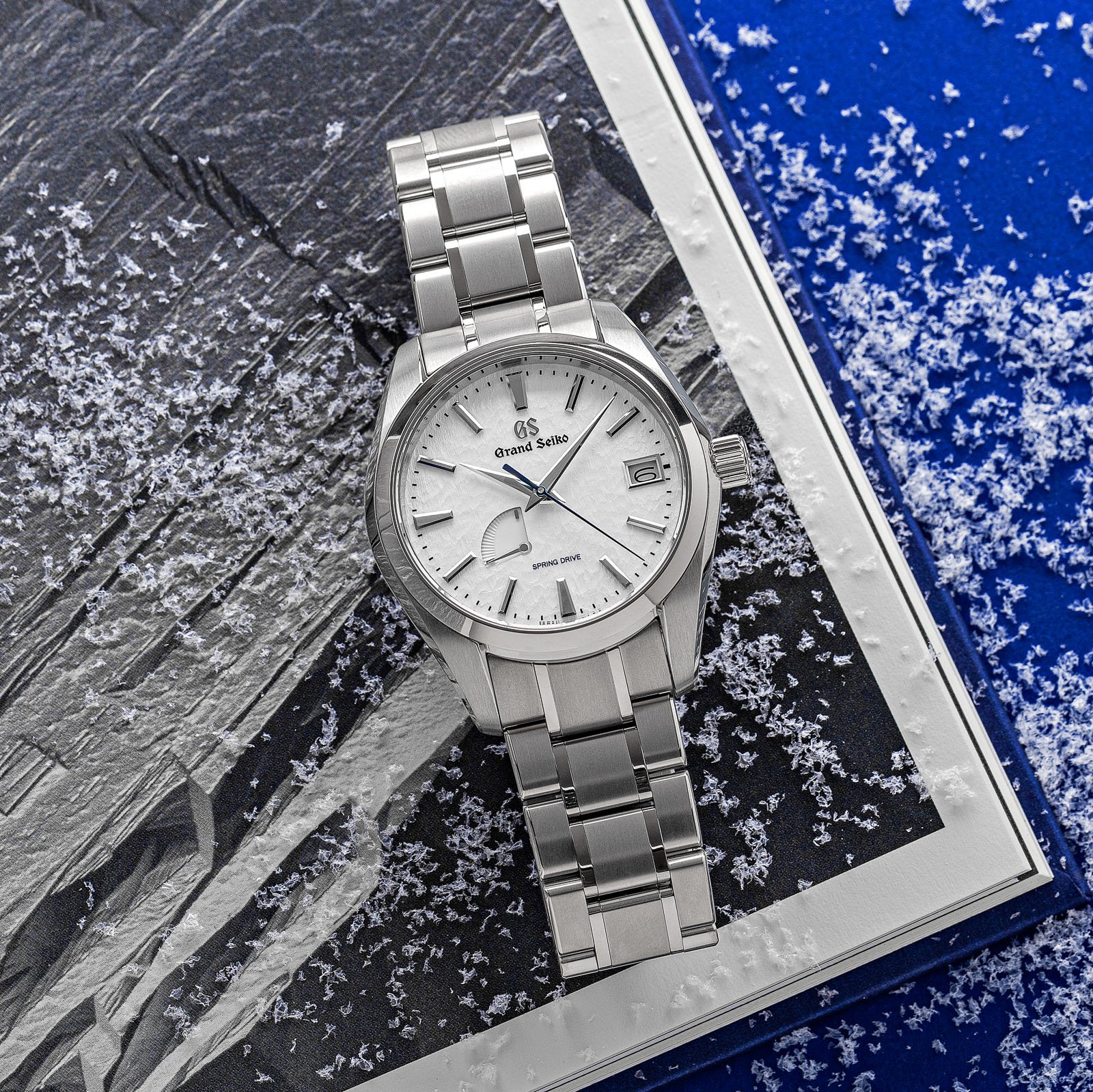 Grand Seiko SBGA211 - titanium wristwatch with a white textured snowflake dial atop a book. 