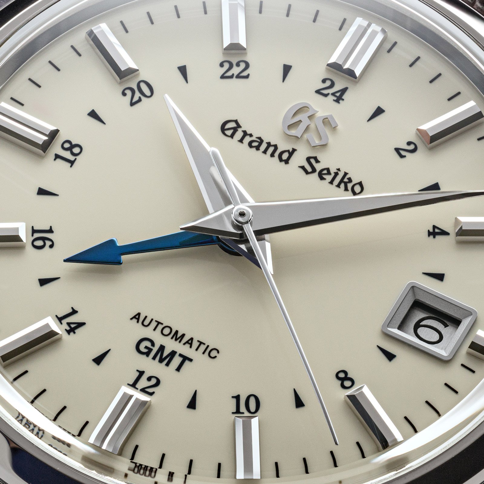 An ivory dial wrist watch with large hands and a blue GMT hand. 