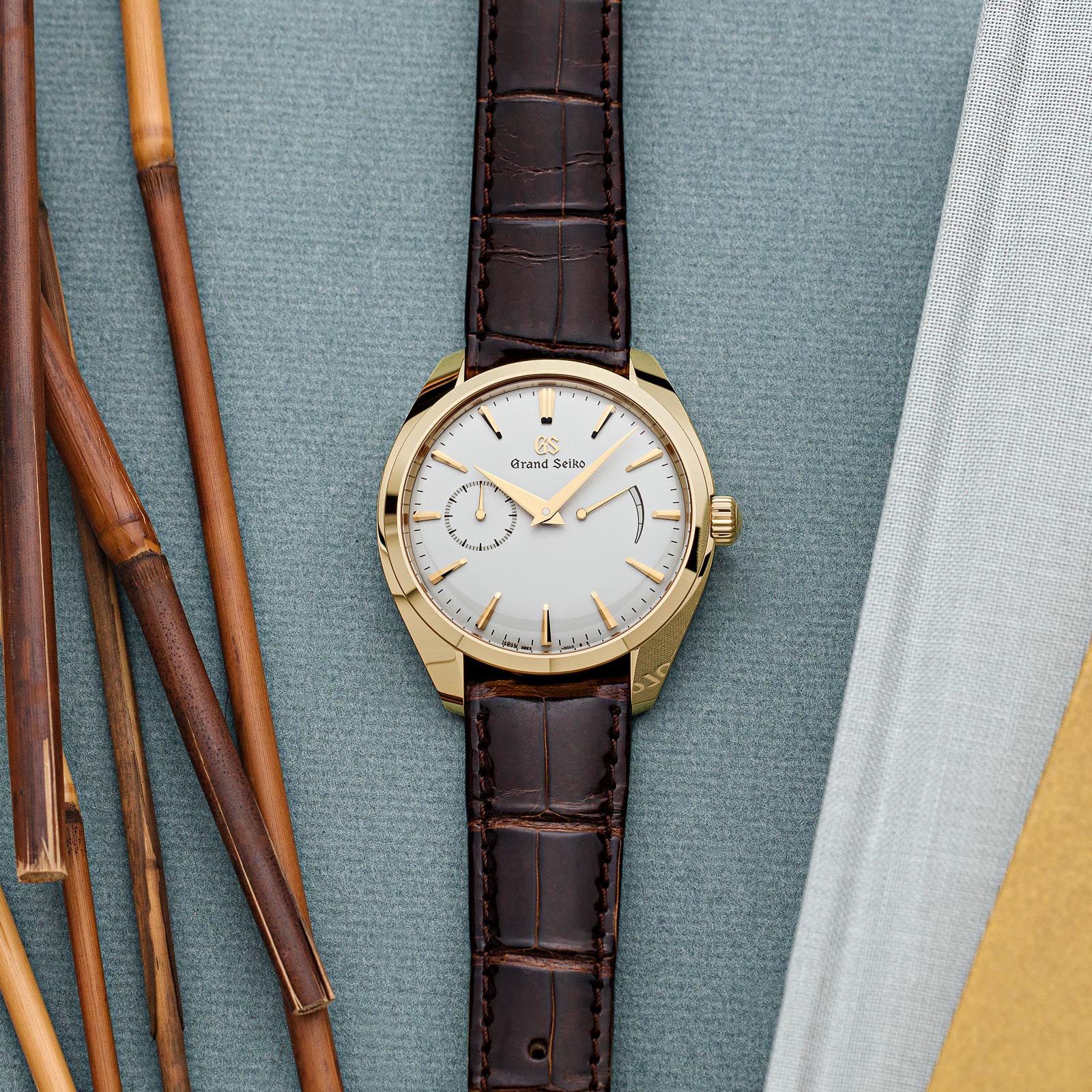 A slim, yellow gold Grand Seiko timepiece with a light dial and brown strap. 