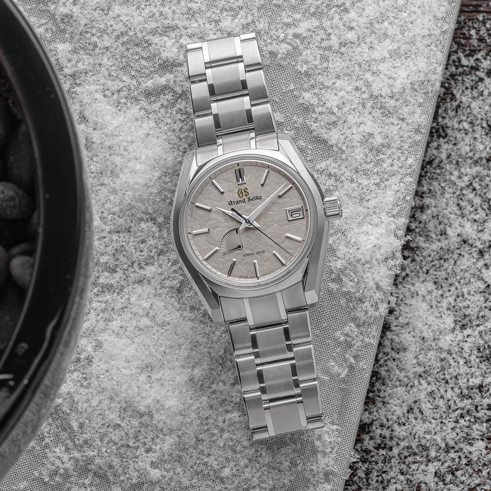 Grey textured dial and titanium case wristwatch with blue and gold-tone accents. 