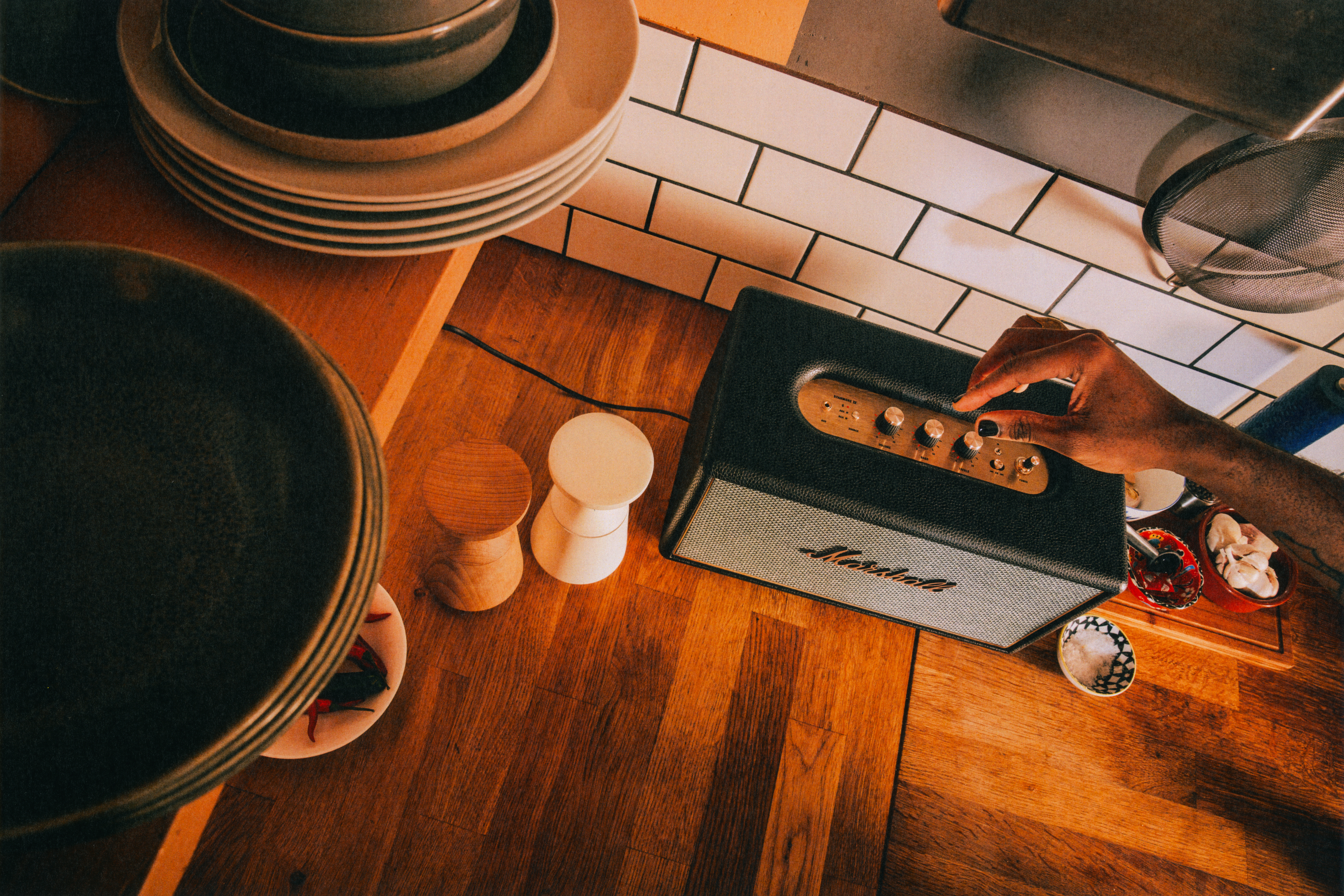 Marshall Stanmore IV Bluetooth speaker on a wooden kitchen countertop, with a person adjusting the controls in a warm, modern home setting.