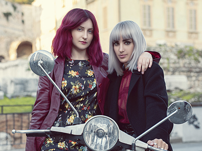 Two women looking at the camera, they are on a scooter