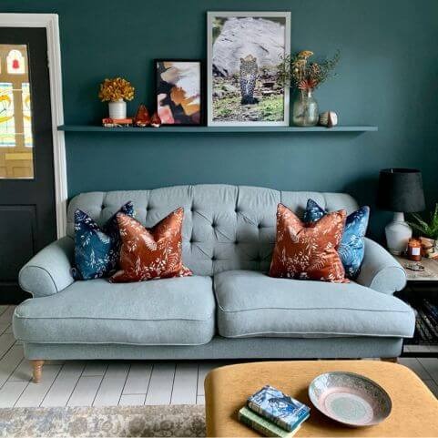 A grey sofa with a pleated button design, decorated with coordinating blue and rust orange floral cushions.