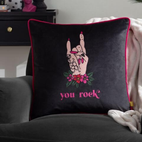 A black velvet cushion with a tattoo-inspired design of a hand and a pink slogan which reads 