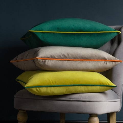 A selection of three velvet cushions with contrasting piped borders, in emerald green, natural mocha and moss yellow shades.