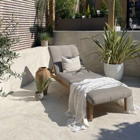 A clean garden space decorated with a grey sun lounger, a woven throw and potted outdoor plants.