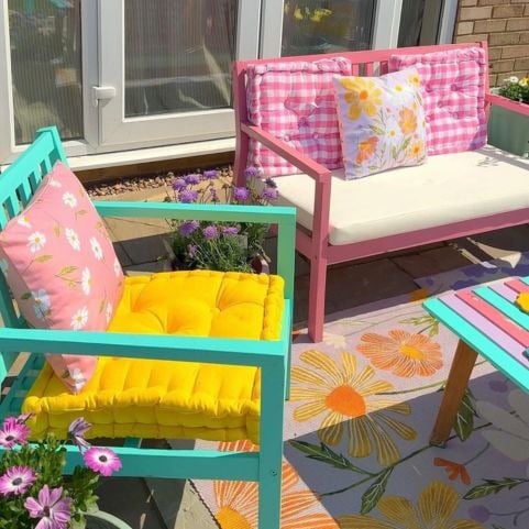 An garden patio seating area decorated with painted wooden benches, colourful seat pads and floral outdoor cushions.