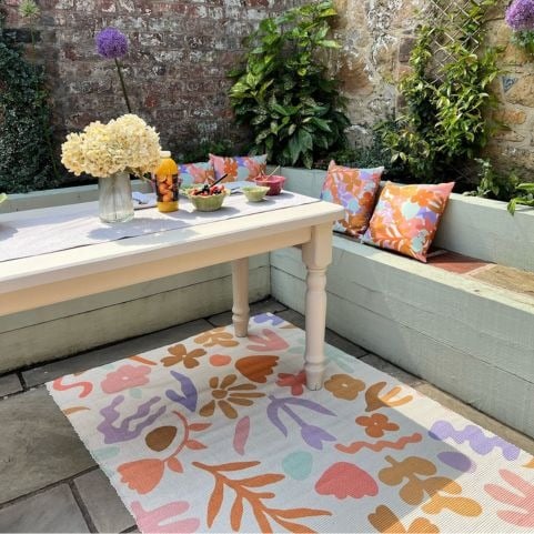 An outdoor seating area featuring upcycled seating, outdoor cushions and an abstract floral garden rug.