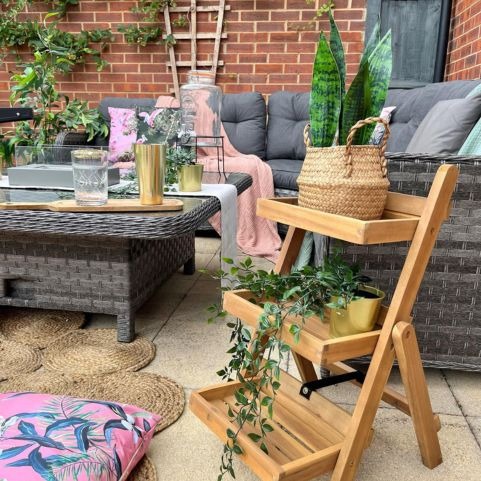 An outdoor seating area decorated with a garden sofa, outdoor cushions, a pink throw and outdoor plants.