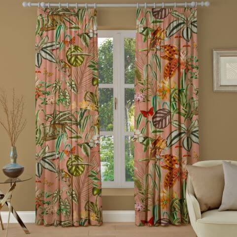 A window dressed with salmon pink patterned curtains. The pattern is jungle themed, with green plants and foliage dominating the pattern. There are butterflies too. 