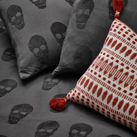 A closeup image of a black duvet cover set with a tufted skull design, with a complementary red and white bed cushion.