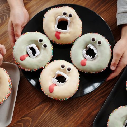 Four Halloween themed donuts decorated with eyes, fangs and fake blood, presented on a black plate laid on a wooden table.
