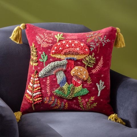 A decorative red pillow featuring colorful embroidered mushrooms and plants