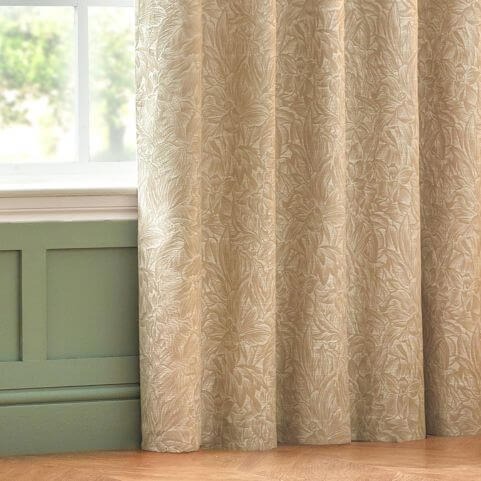 A natural beige coloured curtain panel with a jacquard floral design, opened to reveal a green wall and a window.