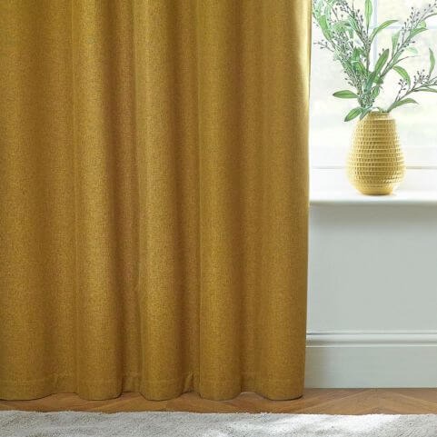 A 100% blackout curtain panel in a vibrant yellow shade, opened to reveal a white wall and window sill holding a potted plant.