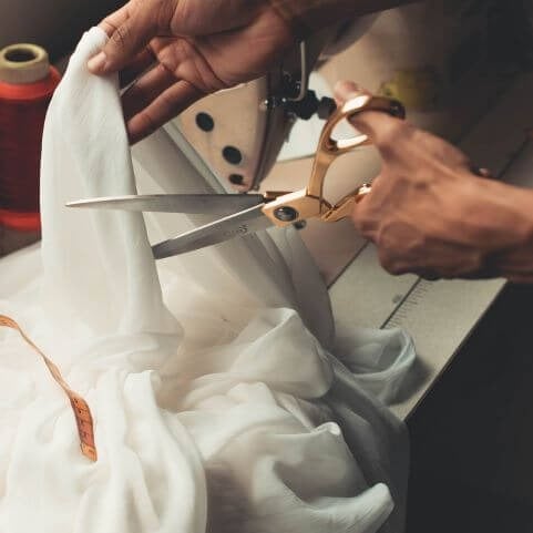 A person holding a large set of gold and silver scissors, cutting a piece of sheer white fabric.