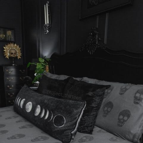 A charcoal Halloween duvet cover set with a tufted skulls design, made on a bed with black bed cushions, a black headboard and black walls.