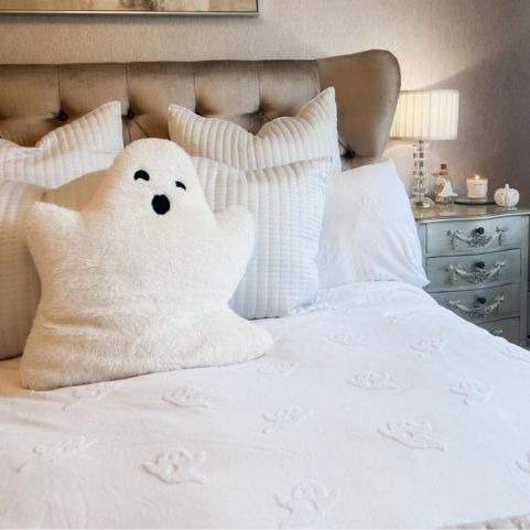 A bedroom with a subtle Halloween theme, including a white tufted ghost duvet cover set and a coordinating ghost plush toy. 