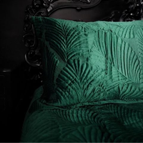 A closeup image of an emerald green pillowcase with an embroidered quilted velvet design, arranged on a matching duvet cover in an all-black bedroom.