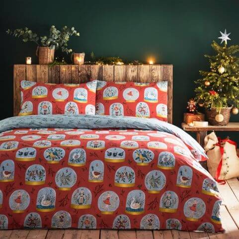 A red Christmas duvet cover set with a printed snow globe design capturing the Twelve Days of Christmas, presented in a green bedroom with lots of festive decor.