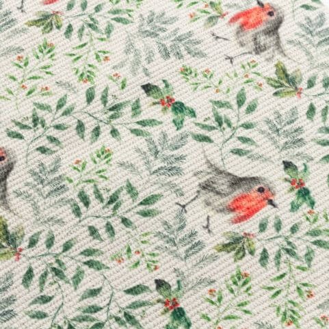 A closeup of the fabric of a Christmas table runner with a printed design of robins and festive foliage.