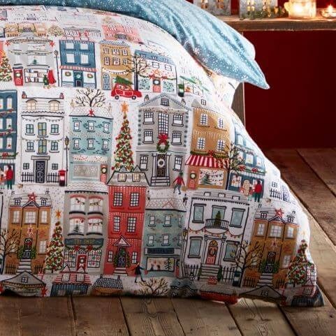 A closeup image of the festive town design on a Christmas duvet set, featuring Christmas trees, townspeople, houses, shops and more.