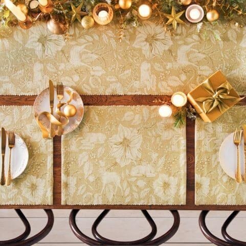 An aerial view of a Christmas table decorated with gold stag placemats, a matching gold stag table runner, candles, cutlery and festive trinkets.