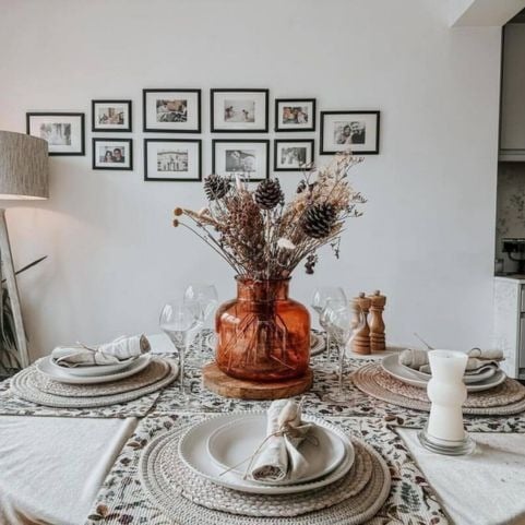 A dining table in a neutral white room, decorated with natural foliage, serviettes and table linen with a festive robin design.
