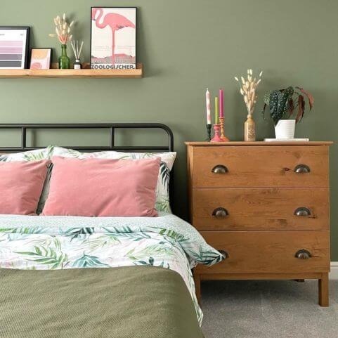 An earthy green bedroom decorated with floral bedding, pink rectangular cushions and various ornaments.