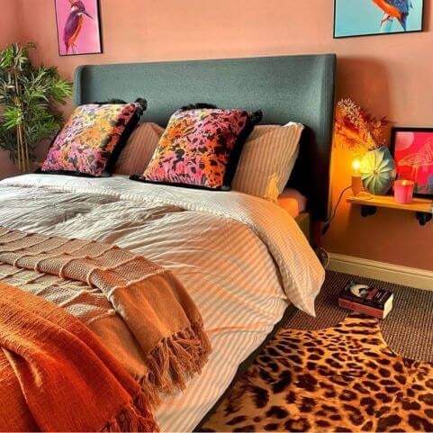 A warmly lit bedroom with a striped duvet cover set, knitted throw blankets and vibrant pink, orange and black scatter cushions.