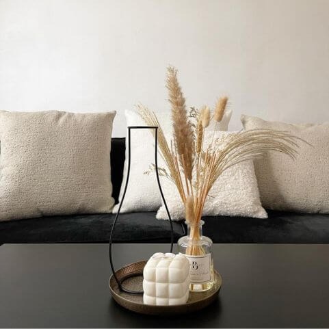 A black fabric sofa decorated with four white and beige bouclé scatter cushions, behind a black coffee table with various ornaments on a metal trey.