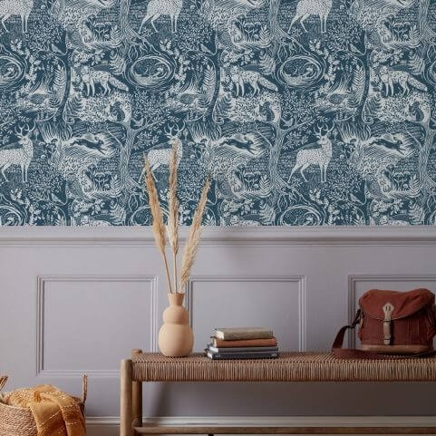 Blue wallpaper with a winter design of woodland foliage and fauna, hung in an entrance hall behind a woven bench holding various ornaments and a woven storage basket on the floor.