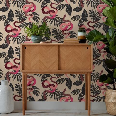 Feature wallpaper with a statement design of pink and black snakes, hung in a room behind a storage table covered with various ornaments.