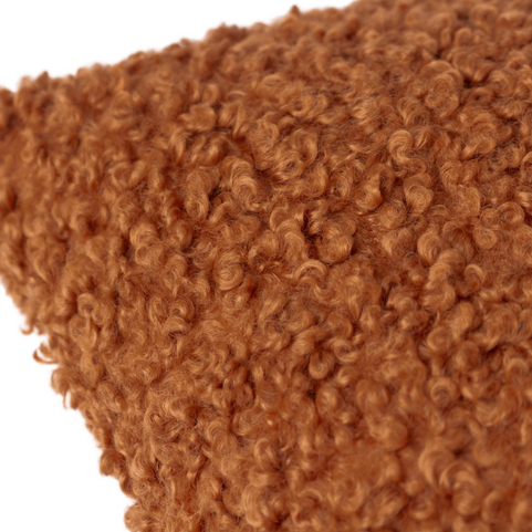 A closeup shot of a woolly bouclé cushion in a ginger shade.