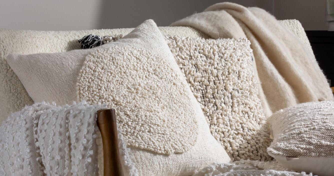 A collection of white bouclé cushions and throws, arranged on a white bouclé sofa.