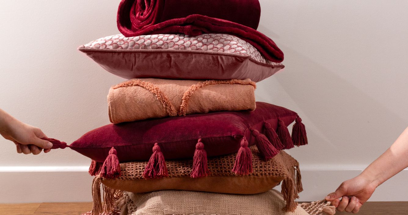 a pile of cushions in red, pink and beige tones.