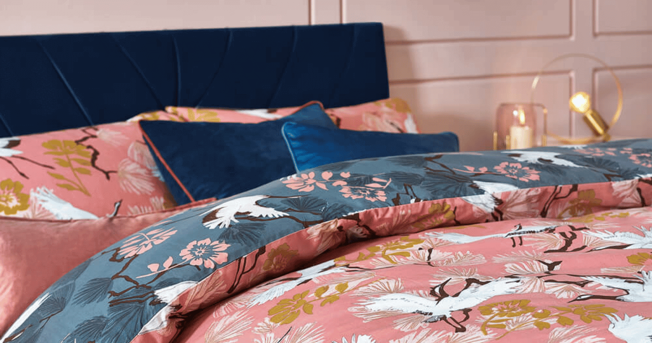 a bed with Demoiselle pink botanical bedding with blue velvet cushions and a blue velvet headboard. 