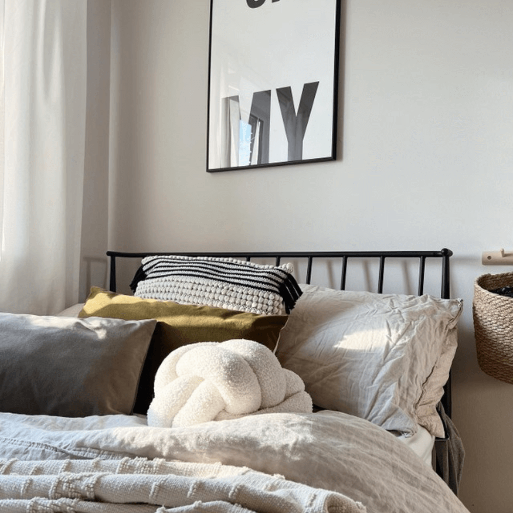 a bed layered up with boucle cushions, linen bedding and knitted throws, all in neutral colours.