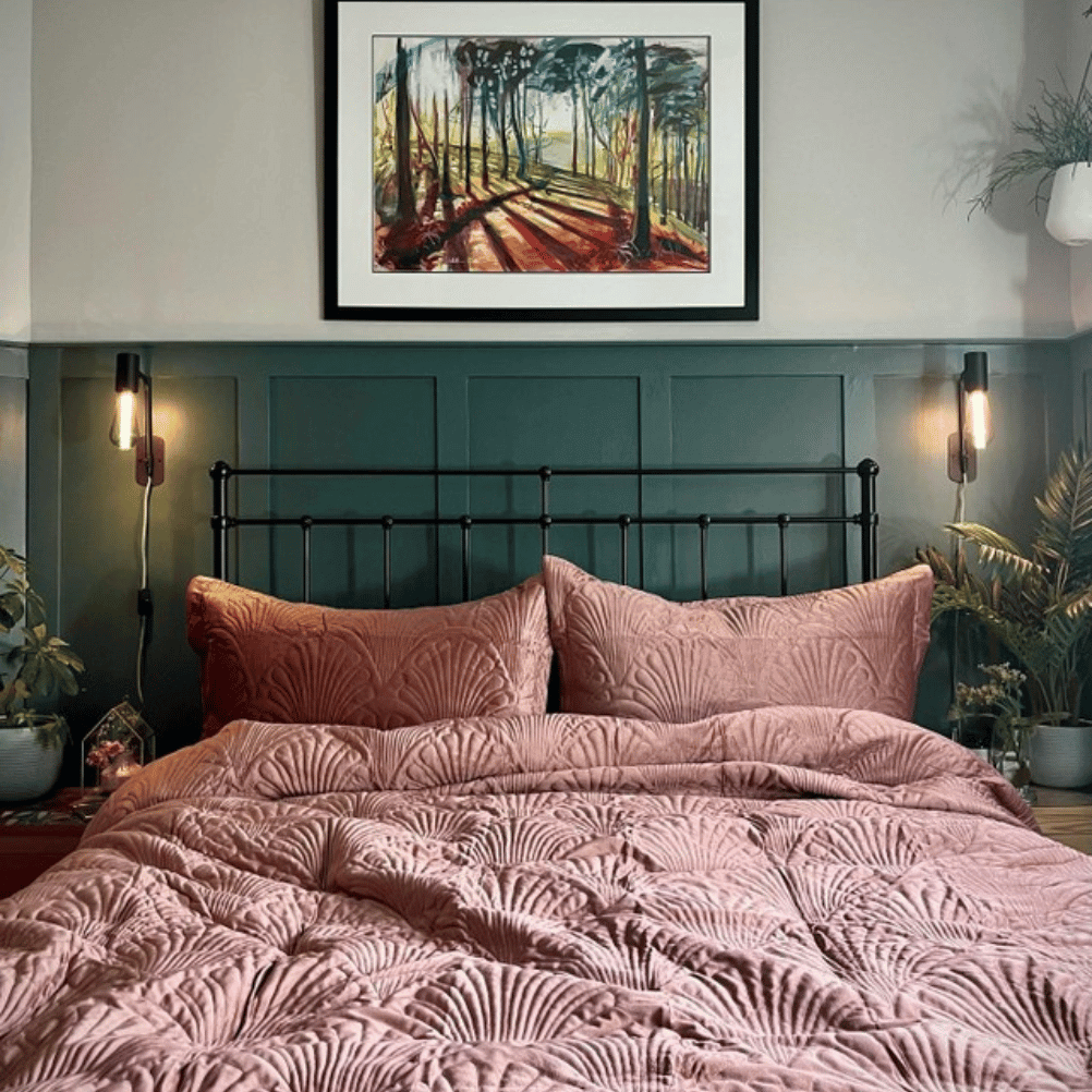 A quilted velvet bedspread in blush pink on a metal frame bed. There's panelling on the wall and it's painted teal. 