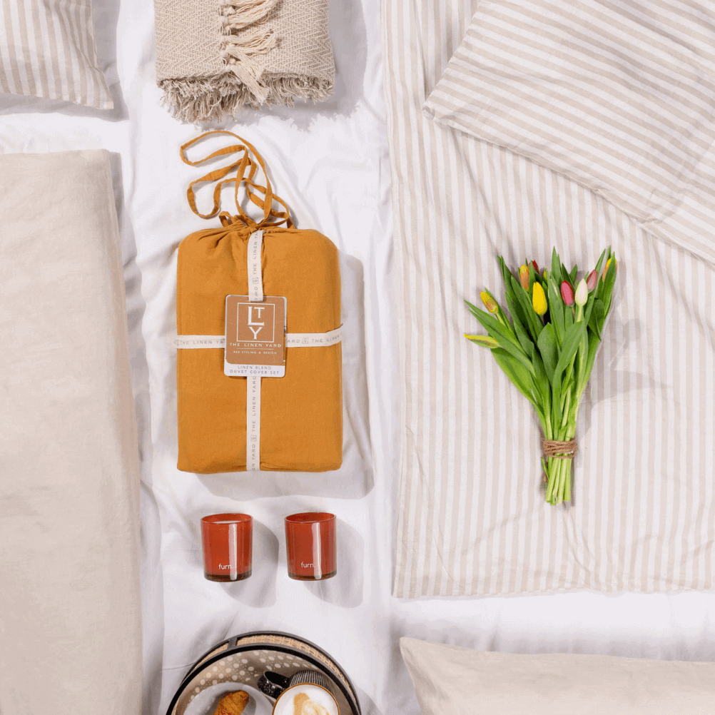 a flat lay of relaxed, scandi style interiors, including subtly striped bedding, natural throws and a bunch of tulips. 