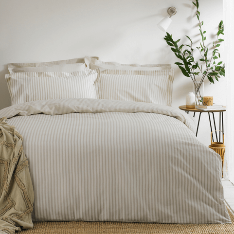 a bed with hebden melange stripe duvet cover on it in natural, styled with a throw on the corner and eucalyptus leaves in a glass on the bedside table. 