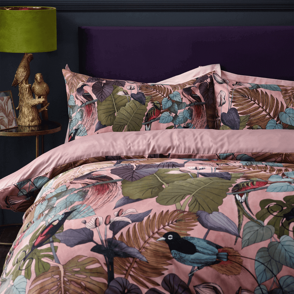 the pink, tropical pattern moriyo duvet cover set on a bed with a purple headboard, next to a parrot lamp base with a green shade. 