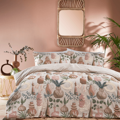 a beige duvet cover set illustrated with ceramic pots and potted plants, in a pale pink coloured bedroom, with a wooden mirror on the wall and ceramic ornaments on a side table.