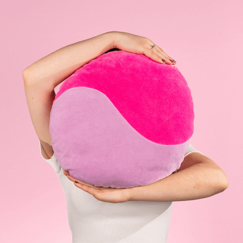 a pink and lilac yin-yang pattern cushion being held between the arms of a person.