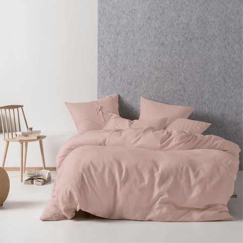 a blush pink linen duvet cover set on a double bed in front of a grey and white wall.