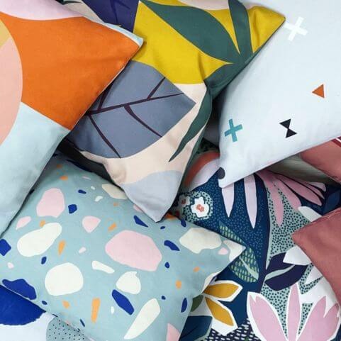 A selection of brightly coloured recycled cushions with floral and abstract designs.