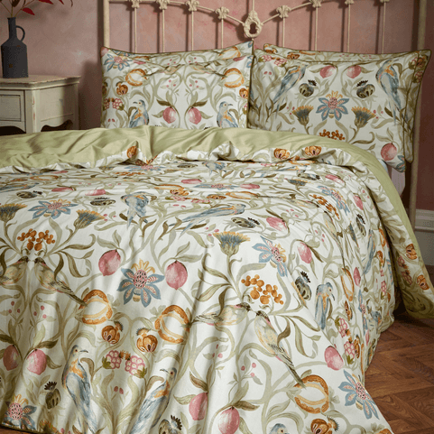 a bed with a pale green bedding on it. it has a heritage pattern on it too. the bed has an ornate metal headboard.
