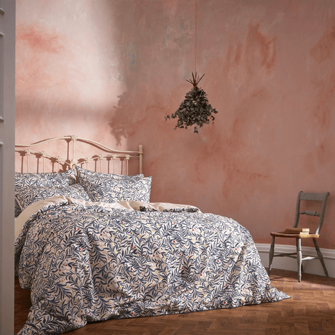 a bedroom with pink limewashed walls. there's an ornate metal framed bed with a navy and blush leafy pattern on it. 